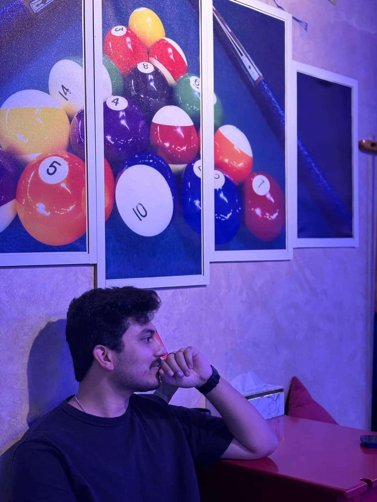 Ritesh at a pool hall, chin in hand, under prints of pool balls